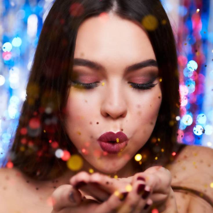 Rosto feminino assoprando confetes exibindo sua maquiagem de festa